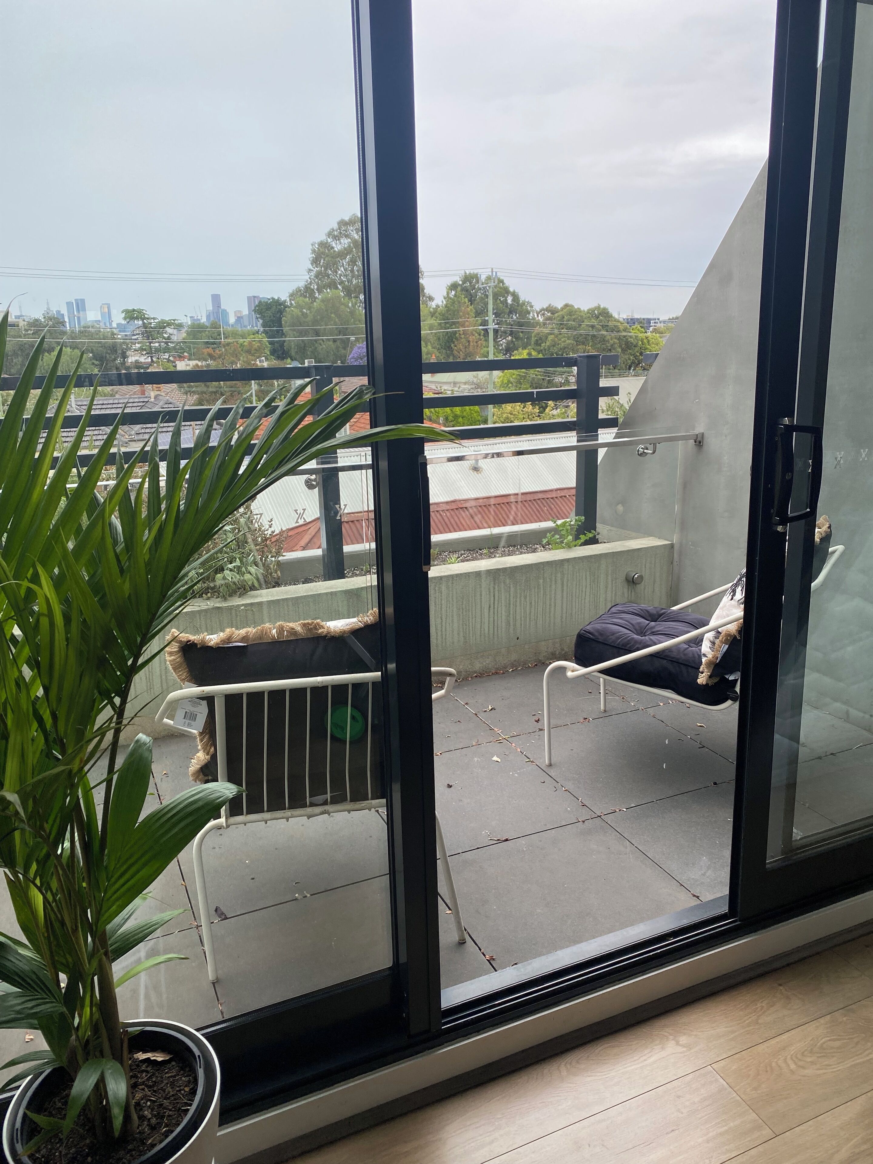 A balcony with a view of a cityscape, a potted plant, and a metal railing.