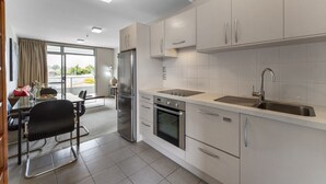 A modern kitchen with stainless steel appliances, a dining area with a table and chairs, and a view of the outdoors through large windows. - Lake Terrace Apartment (Taupō)