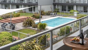 A hotel with a swimming pool, outdoor seating, and a balcony with a table and wine bottle. - Lake Terrace Apartment (Taupō)