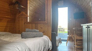 Ein Schlafzimmer einer Holzhütte mit Bett, Stuhl, Schreibtisch und Blick ins Freie.
