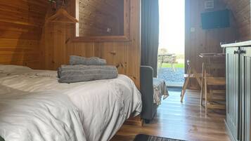 A wooden cabin bedroom with a bed, a chair, a desk, and a view of the outdoors.