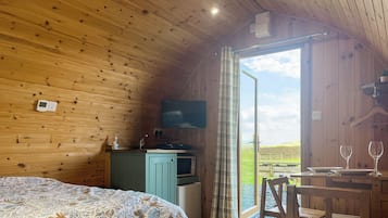 A cozy wooden cabin with a bed, a small kitchenette, a TV, and a table with wine glasses.