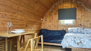 En hyggelig træhytte med en seng, et bord med tallerken og glas, samt en stol.