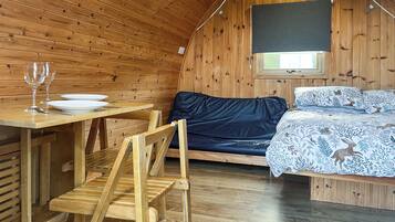 A cozy wooden cabin with a bed, a table with a plate and a glass, and a chair.