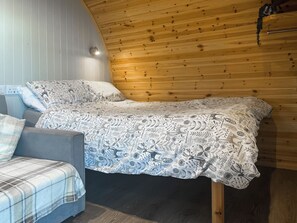 Une chambre à coucher avec un lit recouvert d’une couverture à motifs, un canapé gris avec une couverture à carreaux et un plafond en bois.