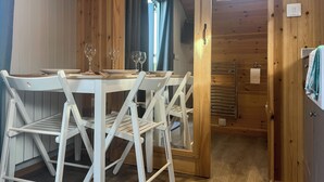 Un interior de madera con una mesa de comedor preparada para cuatro personas, sillas blancas y una ventana con cortinas.