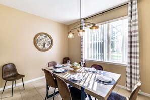A dining room with a wooden table set for four, surrounded by chairs, a chandelier, and a window with curtains. - 9 Mi to Disney: Davenport Home w/ Pool & Game Room (Davenport)