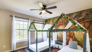Quarto com cama de dossel, ventilador de teto e um mural na parede.