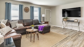 A living room with a brown leather sofa, a coffee table, and a TV mounted on the wall. - 1 Mi to LSU, Tiger Stadium! Lovely Home w/ Parking (Baton Rouge)