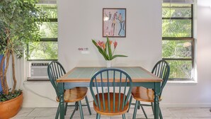 Un área de comedor con una mesa, sillas, una planta en maceta y un cuadro en la pared.