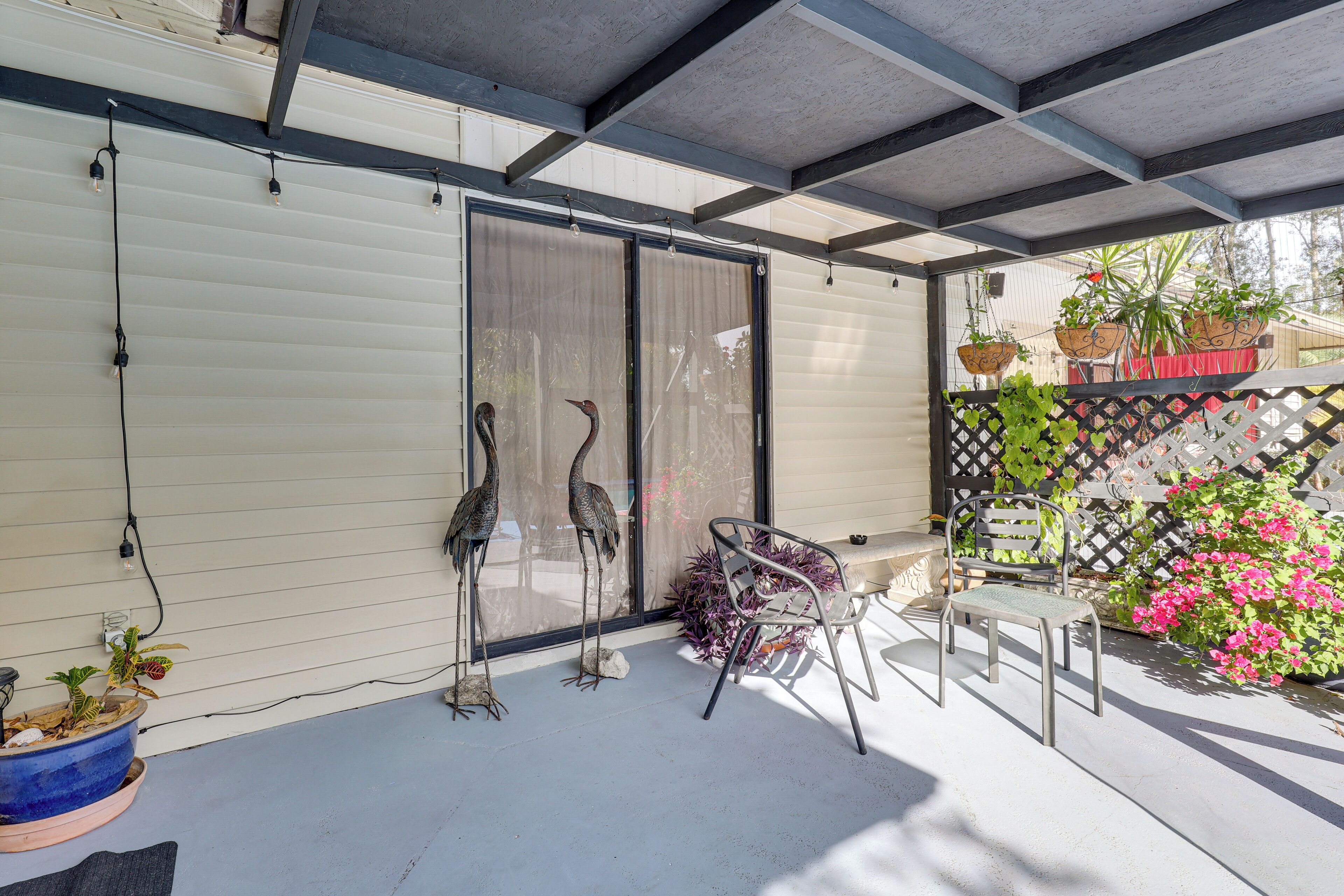 Ein überdachter Patio-Bereich mit einer Schiebetür, einem Metallstuhl und Topfpflanzen.