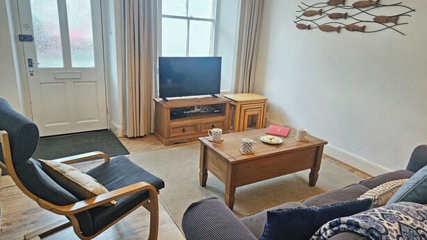 A living room with a sofa, a wooden coffee table, a TV, and a wall art piece. - 2 bedroom accommodation in Looe (Looe)