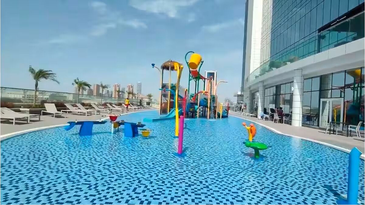 Ein Pool auf dem Dach mit Wasserrutschen und Liegestühlen, umgeben von modernen Gebäuden.