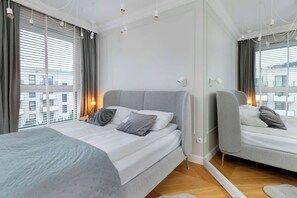 Une chambre d’hôtel moderne, dotée d’un grand lit, d’une table de chevet, d’un miroir et offrant une vue sur la ville grâce à de grandes fenêtres.