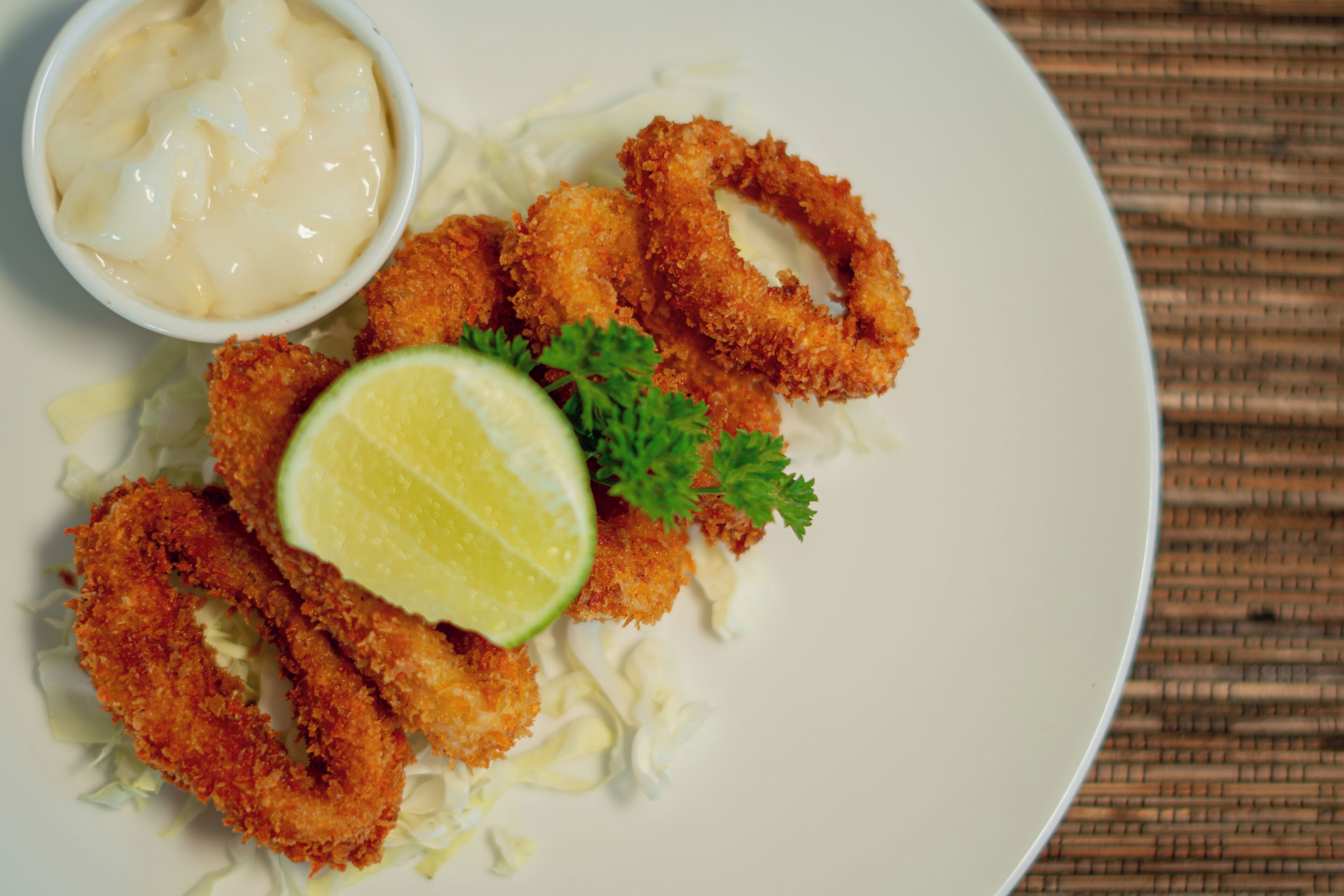 A plate of breaded and fried food items, possibly chicken tenders, with a wedge of lime and a small bowl of sauce.