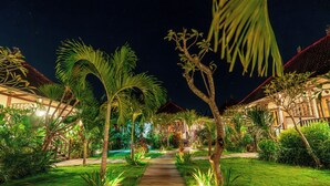 A nighttime view of a garden pathway leading to a building with a red roof, surrounded by palm trees and well-lit plants. - D’Gume Villas Lembongan by Bali Cabin (Lembongan Island)