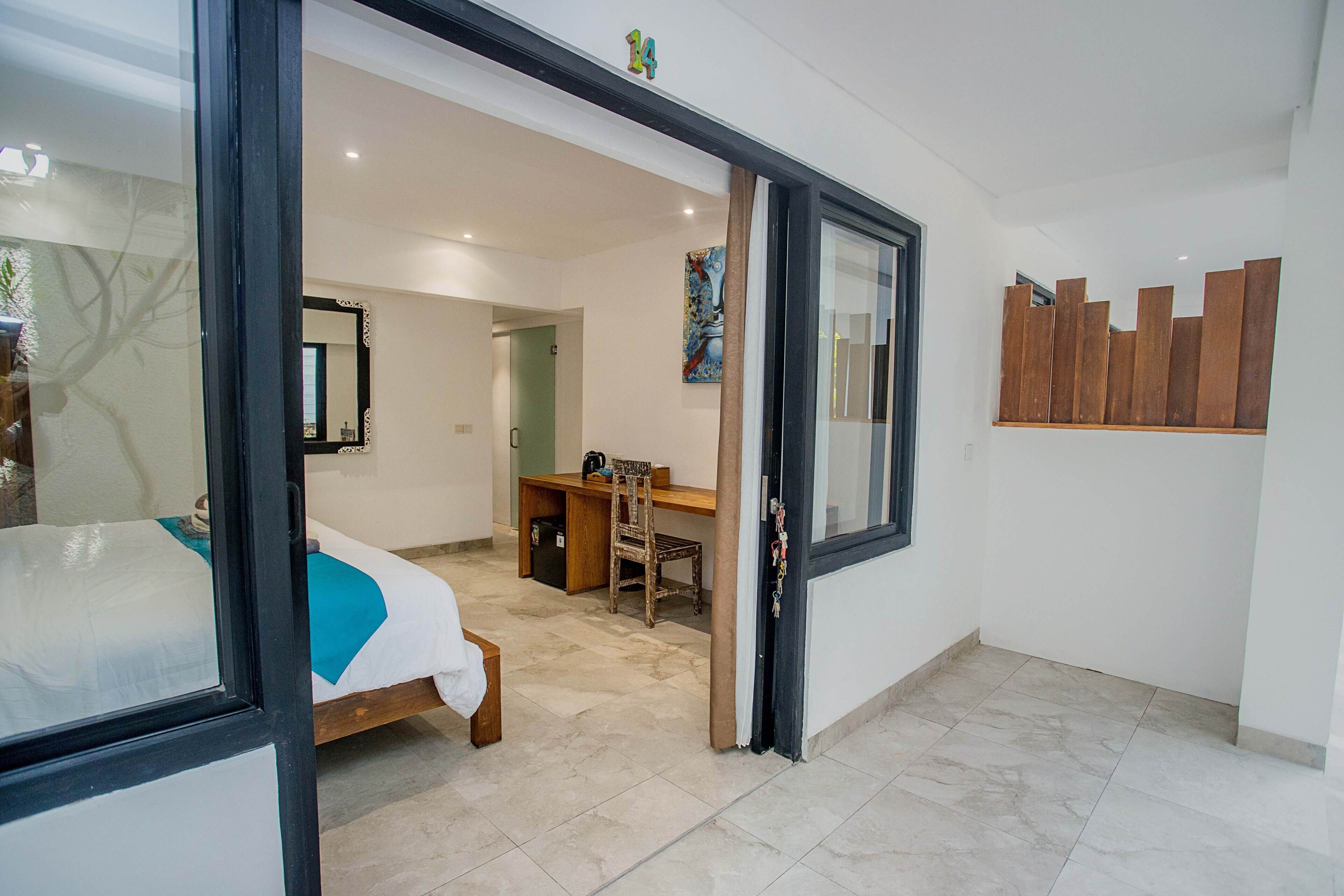 A bedroom with a bed, a desk, and a chair, a bathroom with a mirror, and a wall with a wooden panel.