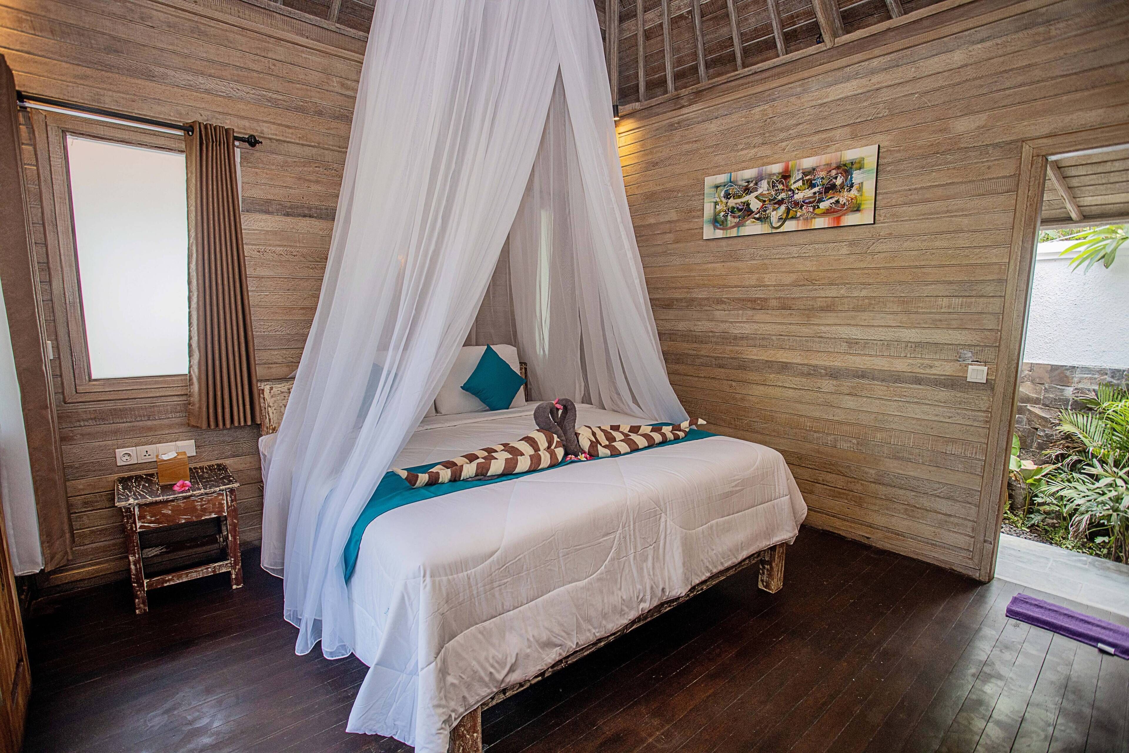 A room with a bed under a canopy, wooden walls, a small nightstand, and a window with curtains.
