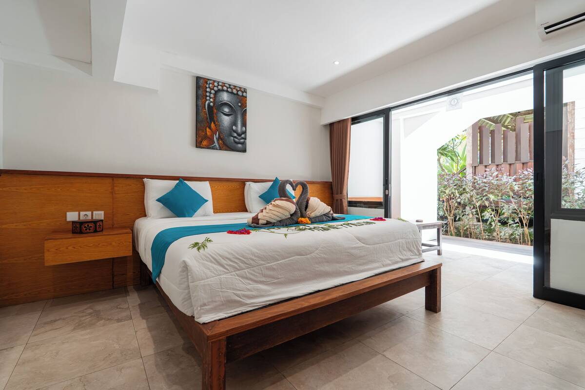 Quarto moderno com cama de madeira, mesa de cabeceira, obra de arte na parede e vista para um jardim através de uma porta de vidro.
