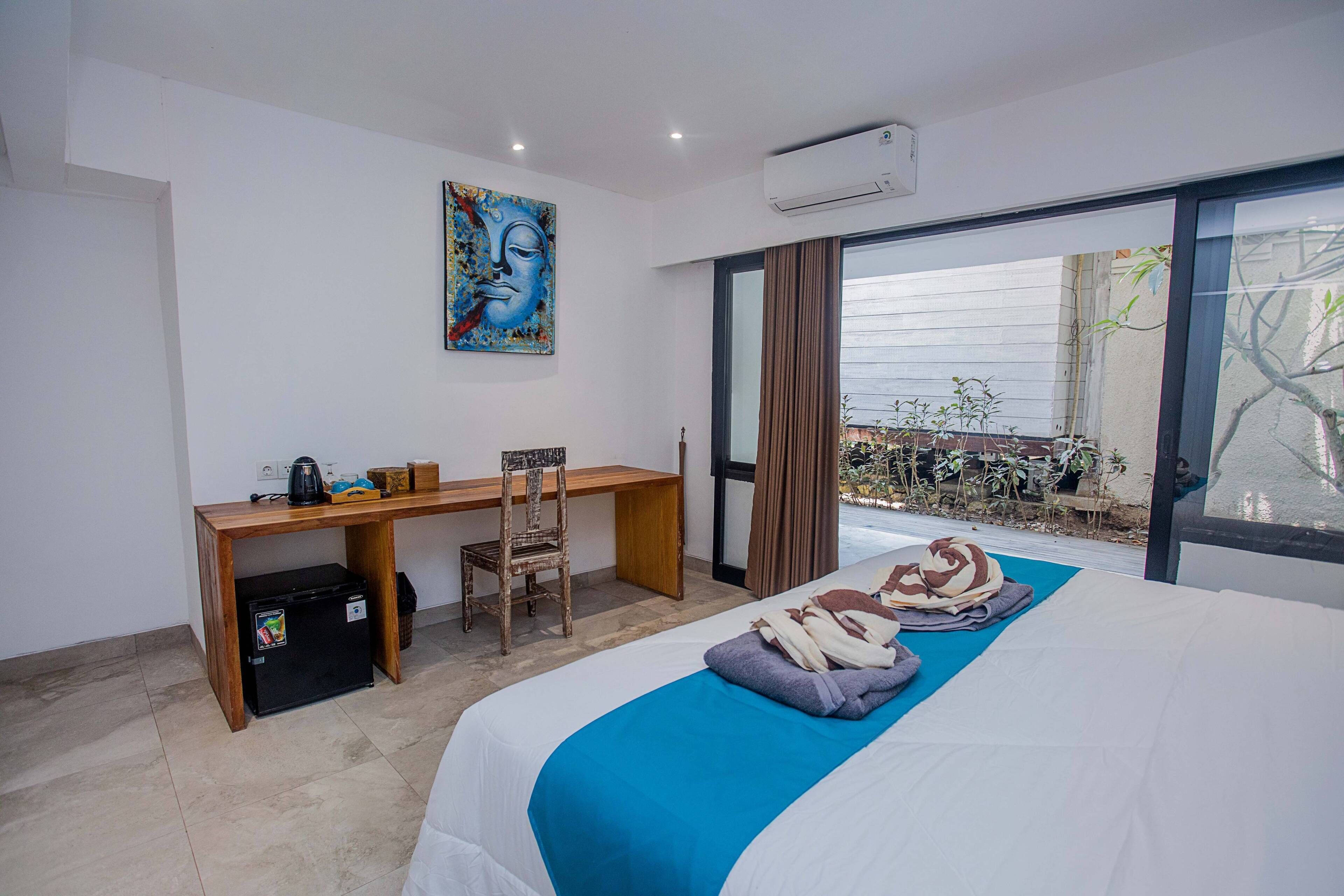 Una habitación de hotel con cama, escritorio, silla y un refrigerador pequeño.
