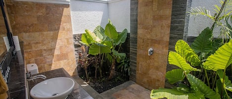 A bathroom with a white sink, a shower, and large green plants.