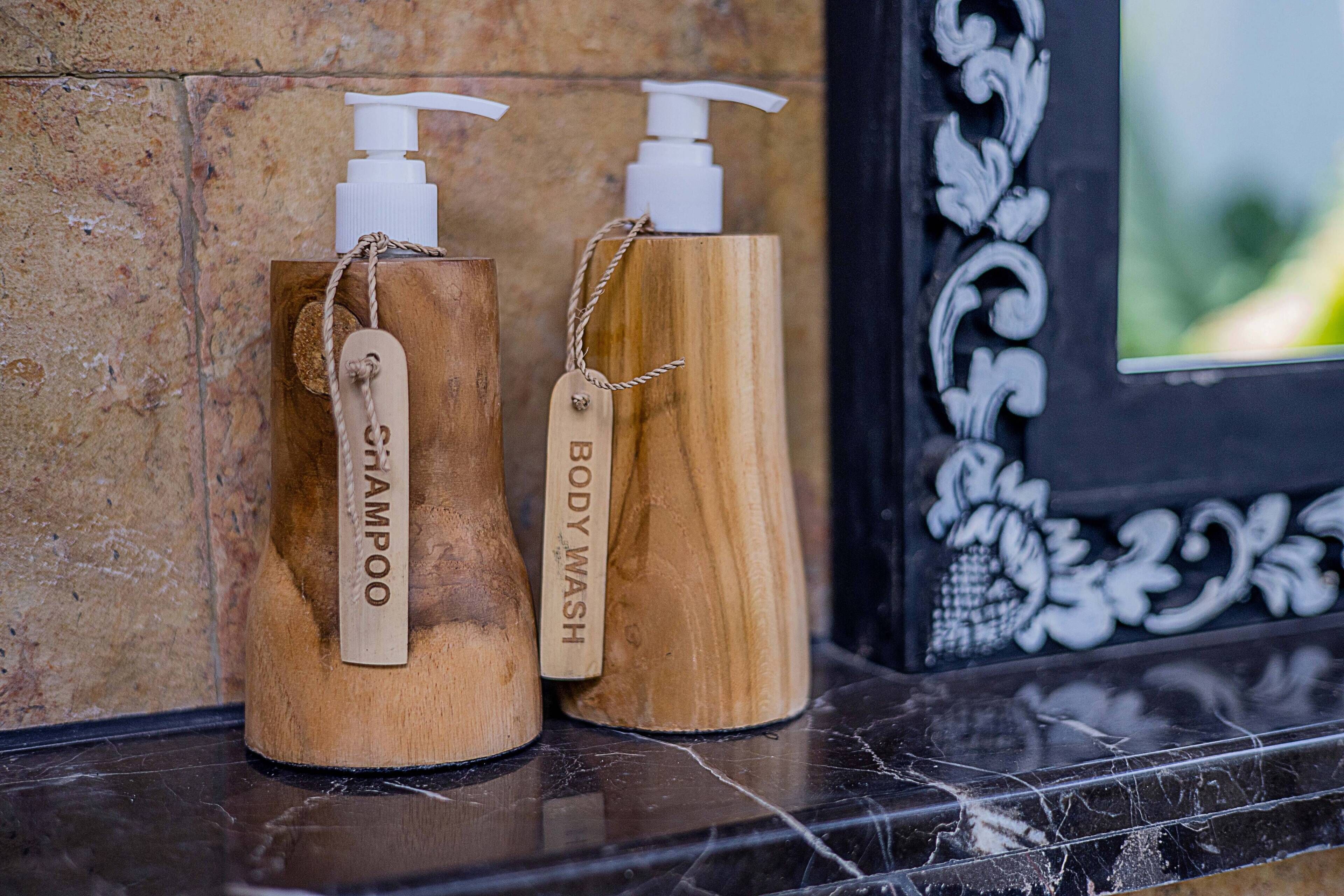 Dos botellas de madera con dosificadores, etiquetadas 'champú' y 'gel de baño', sobre una superficie de mármol.