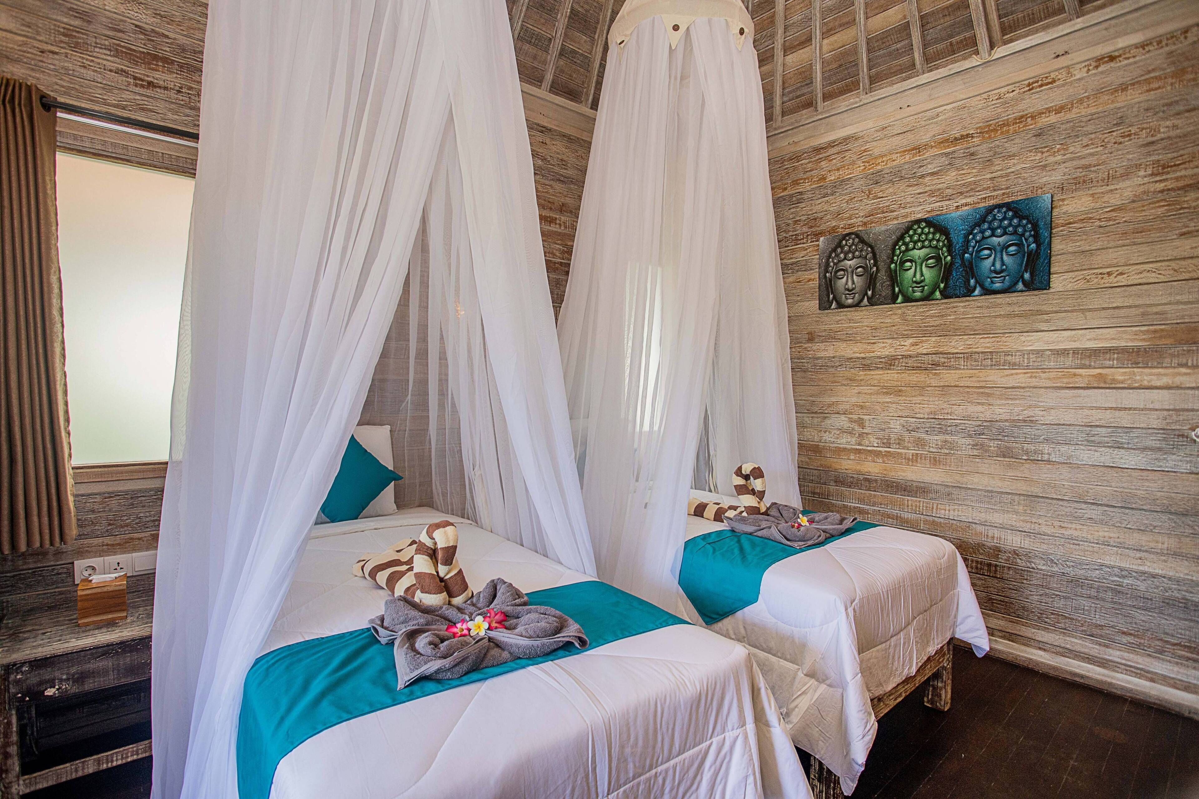 A room with two beds, each with a canopy, and a wooden wall with three Buddha statues.