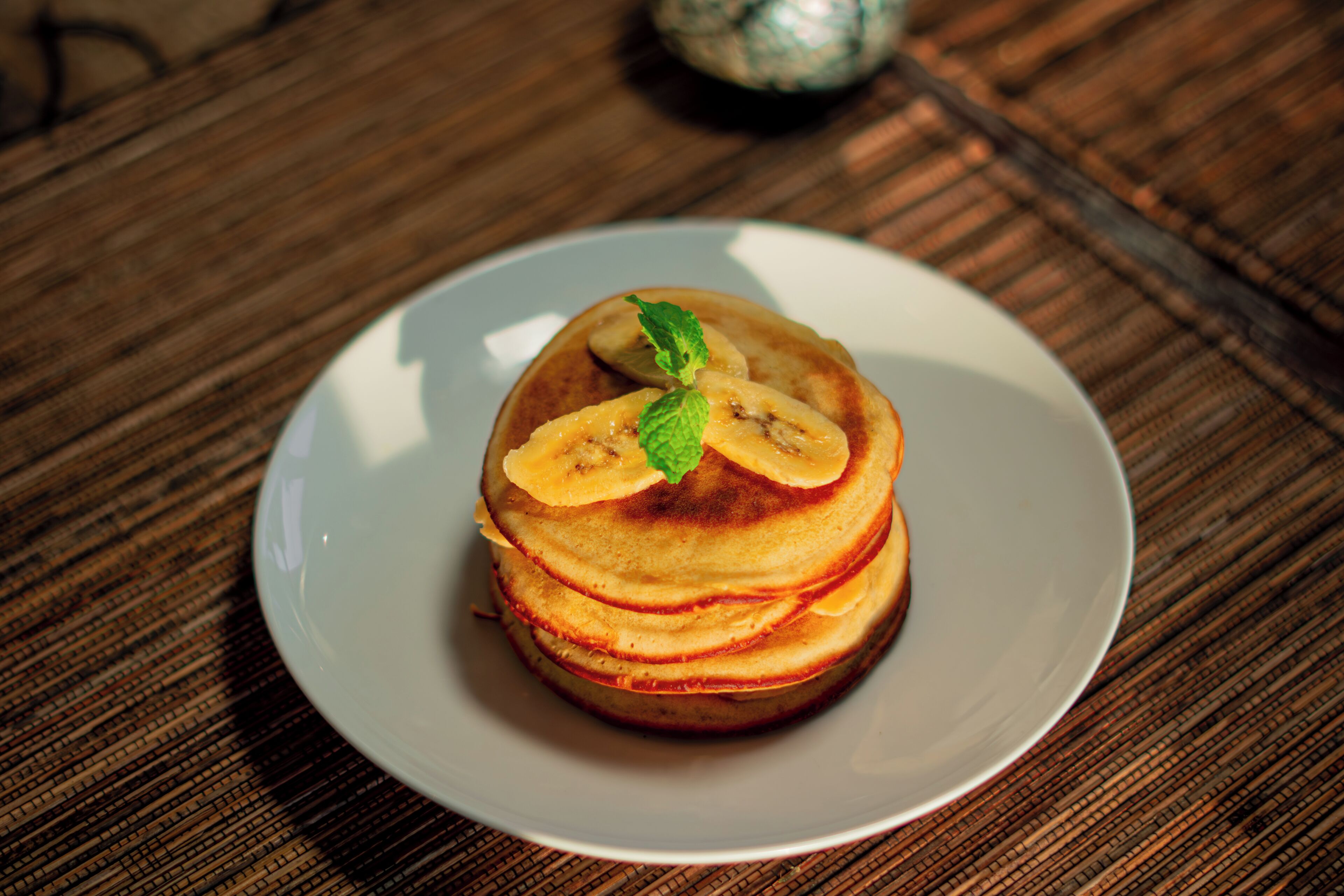 A stack of pancakes on a white plate on a wooden table.