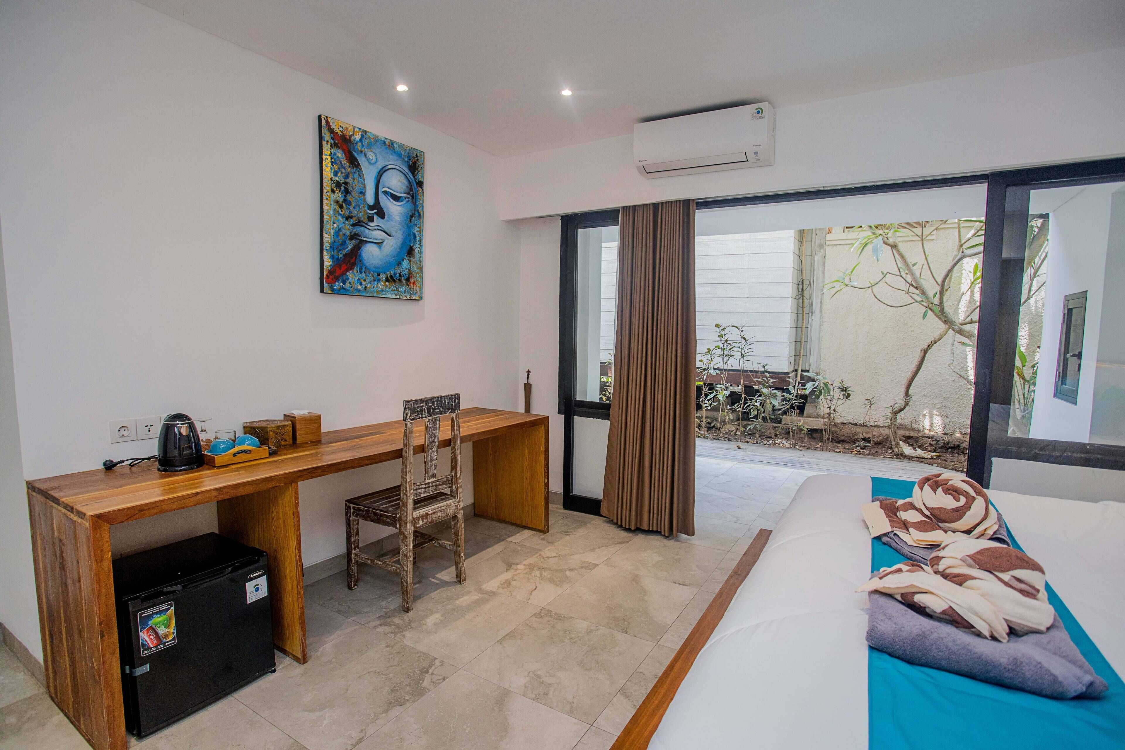 A hotel room with a bed, a desk with a chair, a small refrigerator, and a window with curtains.