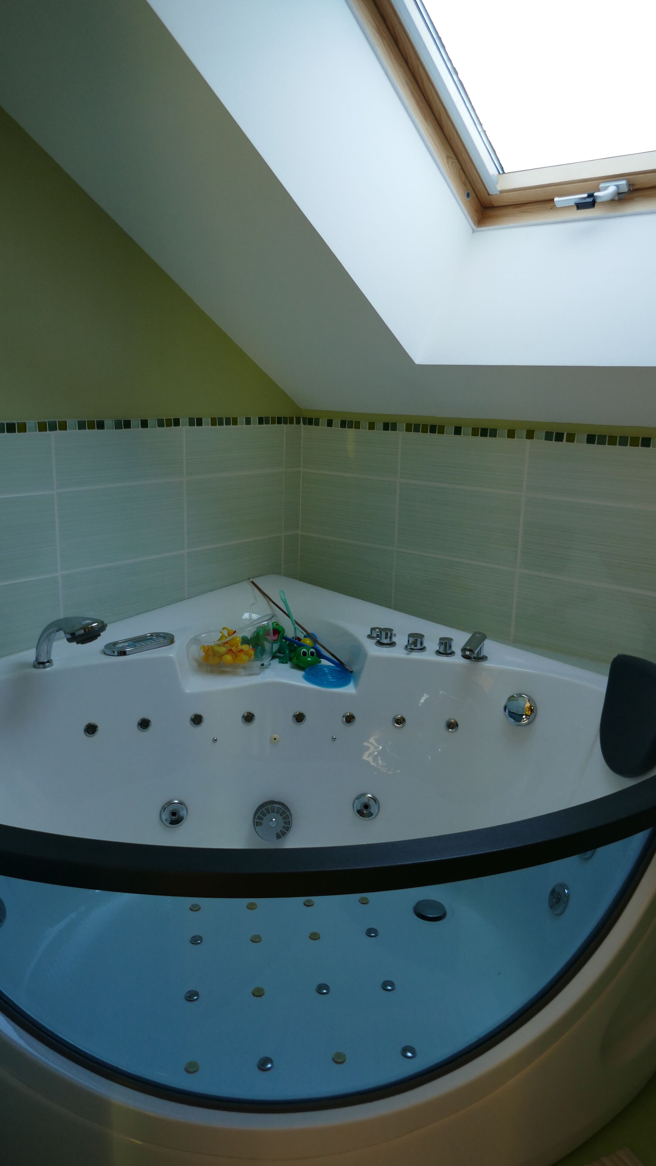 Een badkamer met dakraam, een badkuip met whirlpool en een klein plankje met toiletartikelen.