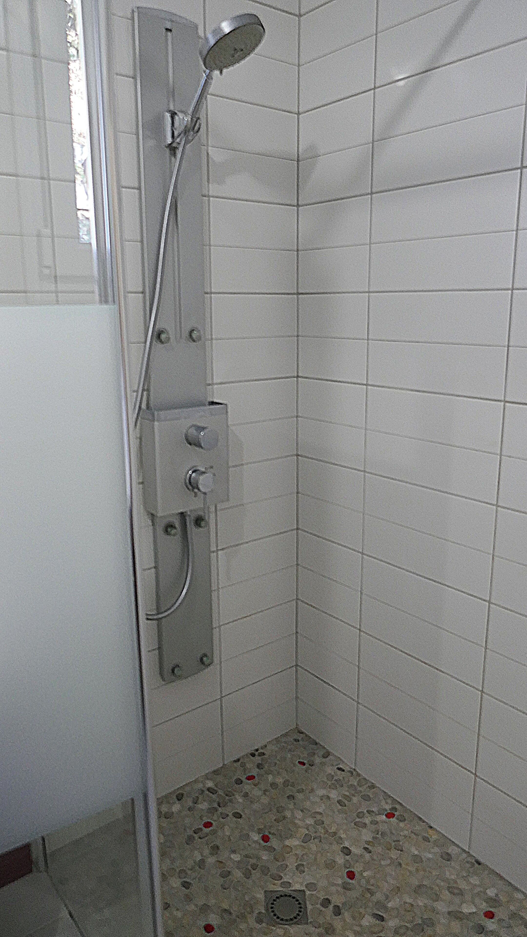 A small, tiled shower area with a handheld showerhead and control knobs.