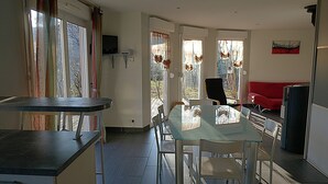 A dining area with a glass table and chairs, a red sofa, and a television on the wall.