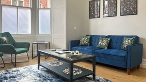 A living room with a blue sofa, green armchair, and a glass coffee table. - Lakes and Shores Retreat (Maryport)