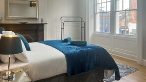 A neatly arranged bedroom with a bed, bedside table, lamp, and a large window offering a view of the outside. - Lakes and Shores Retreat (Maryport)