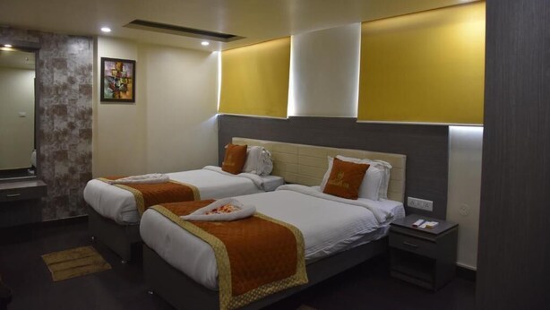 A hotel room with two beds, a small bedside table, a nightstand, and a mirror. - Aalcajars Inn (Patna)
