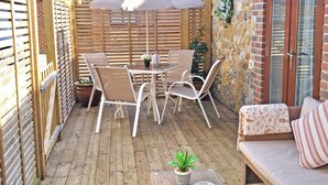 A patio with a table and chairs, a potted plant, and a cushioned seating area. - Rookery Farm Holiday Cottage (Bognor Regis)
