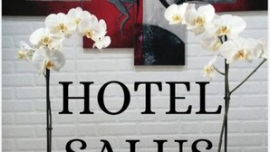 Um lobby de hotel com parede de tijolos brancos, duas orquídeas brancas em vasos e obras de arte abstratas.