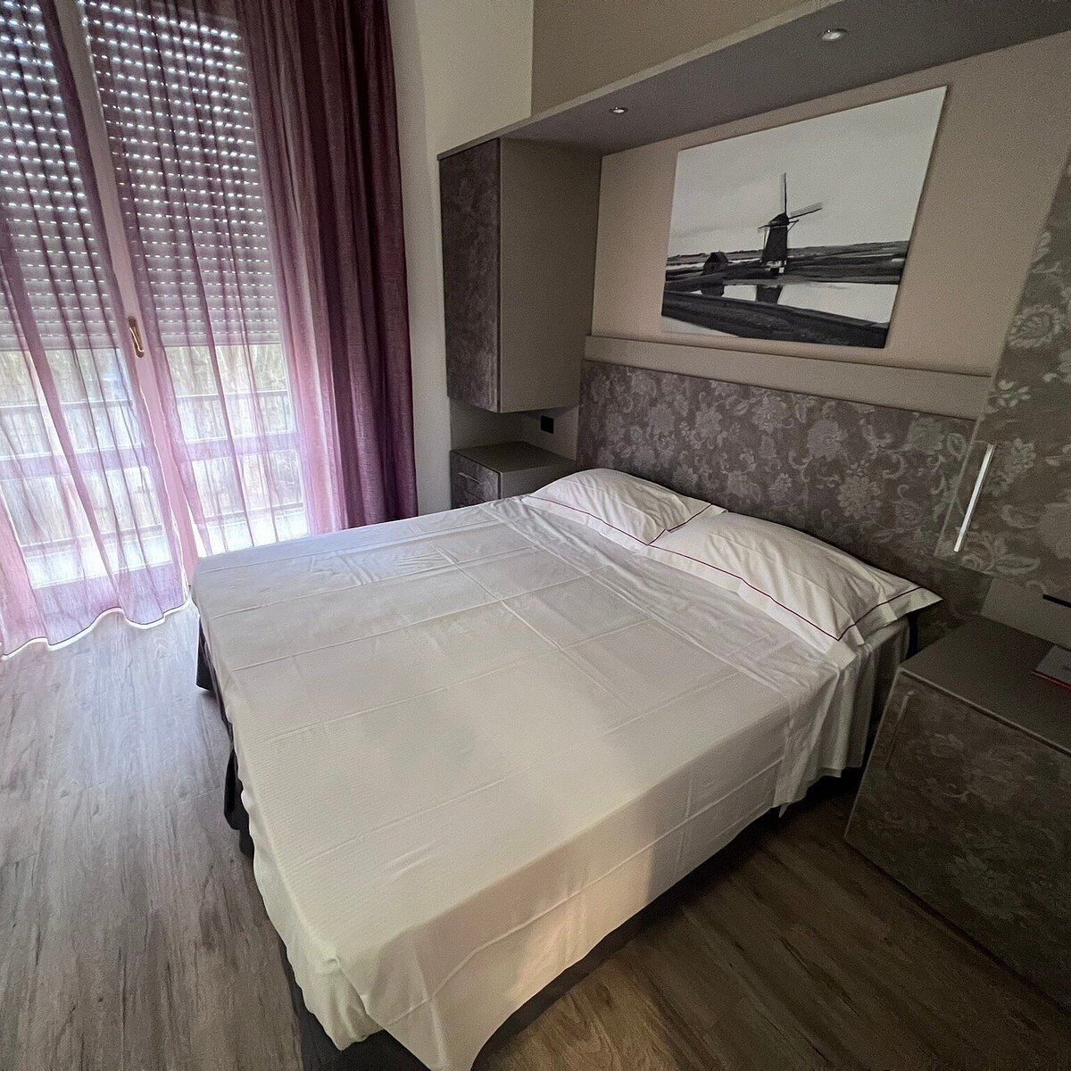 A hotel room with a bed, a nightstand, a mirror, and a window with curtains.
