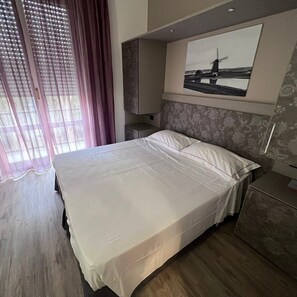 A hotel room with a bed, a nightstand, a mirror, and a window with curtains. - Hotel Salus Milano (Milan)