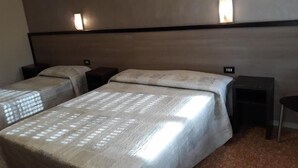 Quarto de hotel com duas camas, cada uma com colcha e almofadas estampadas, flanqueadas por mesas de cabeceira com luminárias.