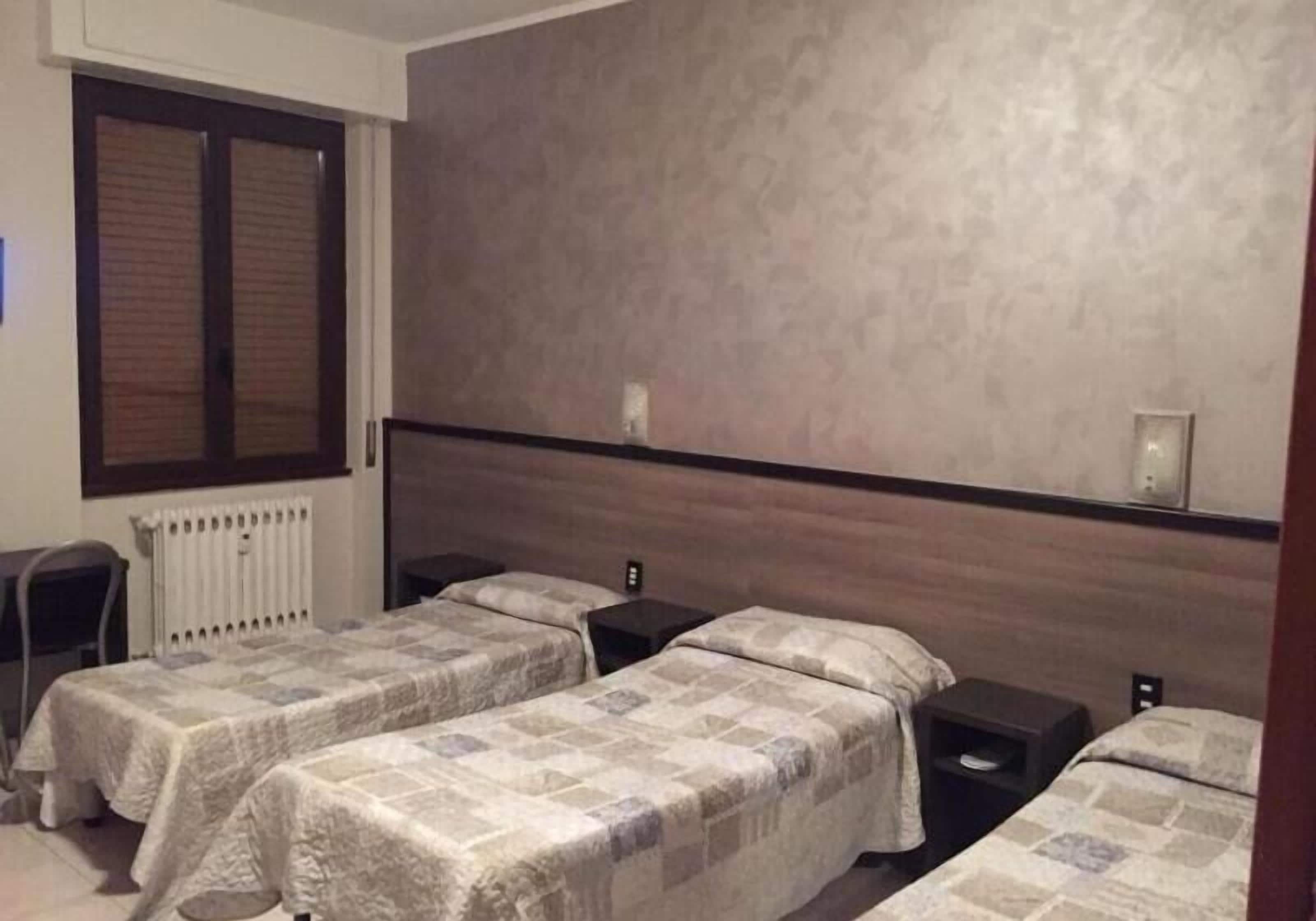 Ein Hotelzimmer mit zwei Einzelbetten, einem Holzkopfteil, einem Heizkörper und einem Fenster mit Jalousien.