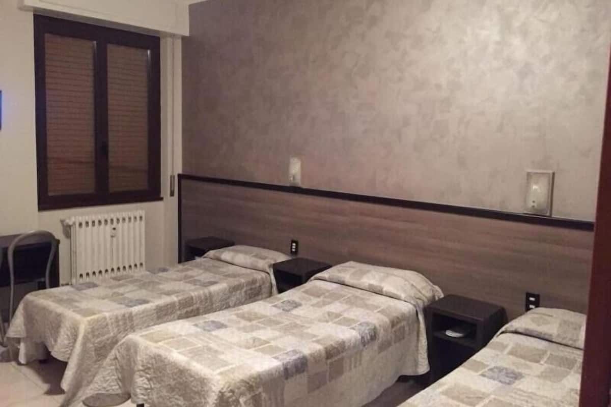 A hotel room with two single beds, a wooden headboard, a radiator, and a window with blinds.