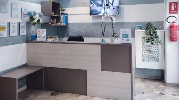 Uma área de recepção com design moderno, apresentando um balcão, assentos e uma televisão montada.