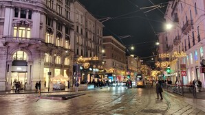 Uma rua histórica com edifícios elaborados, um bonde e luzes festivas.