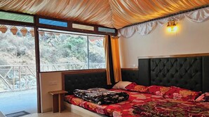 Ein Schlafzimmer mit einem großen Bett, einer Bank und Blick auf eine gebirgige Landschaft durch große Fenster.