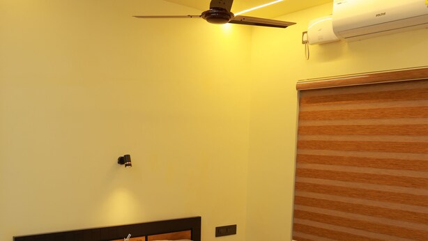 A neatly made bed with a wooden headboard, a ceiling fan, and an air conditioning unit mounted on the wall. - SJ HOMES  (Changanassery)