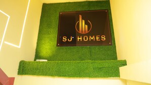A sign with 'SJ HOMES' on a wall with green artificial grass. - SJ HOMES  (Changanassery)