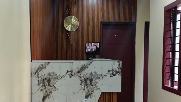 A reception area with a marble counter, wooden paneling, a clock, and a TV screen. - SJ HOMES  (Changanassery)