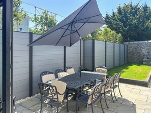 Un patio al aire libre con una mesa y sillas, un gran paraguas y una pared de piedra.