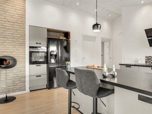 A modern kitchen with a central island, bar stools, a hanging light, and a brick accent wall. - "Muriel" - 1.6km from the sea by Interhome (Blokhus)